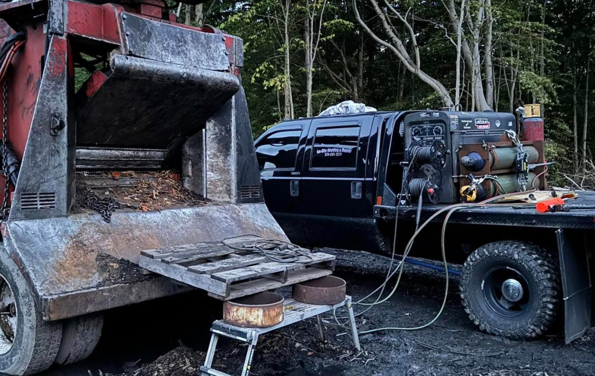 A black truck is parked next to a machine on a trailer.
