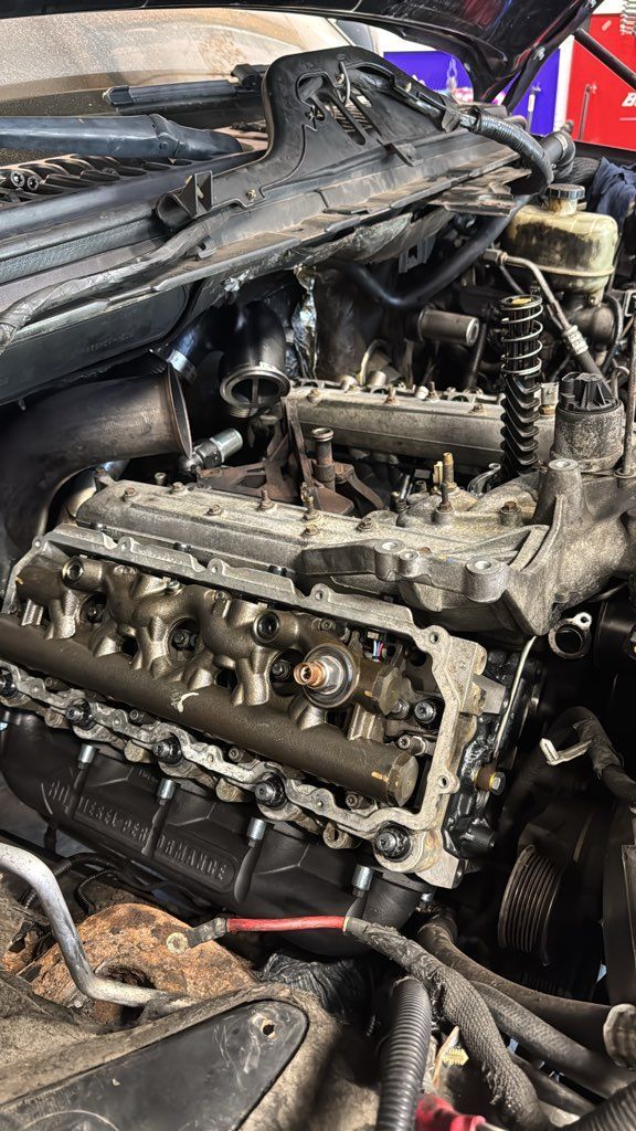 Engine of a vehicle with exposed cylinder heads and various components, likely undergoing repair.