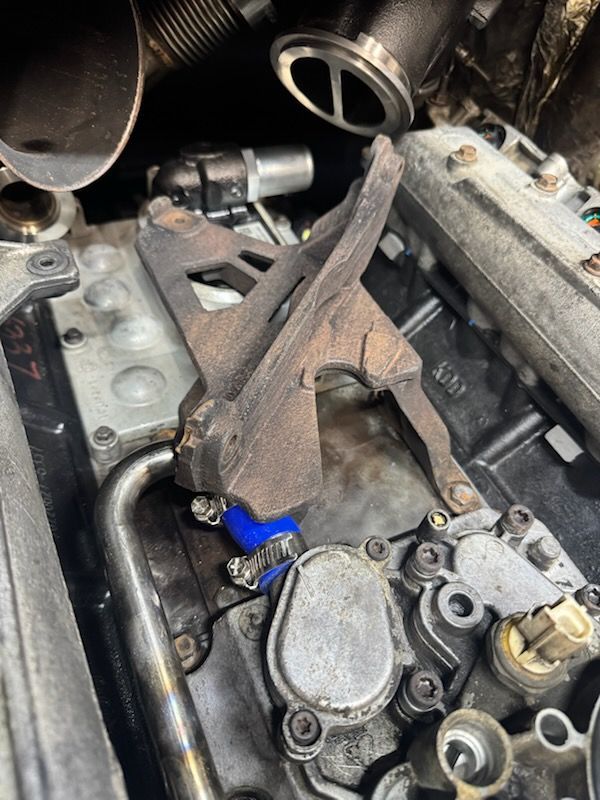 Close-up of engine components with a rusty metal bracket and a blue hose attached.