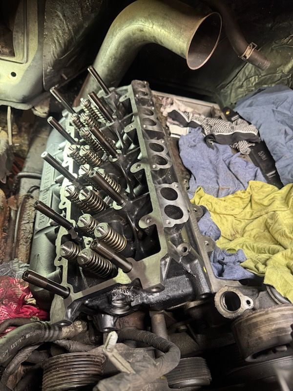 Engine cylinder head being worked on, with valves and springs exposed.