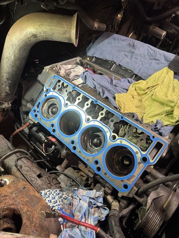 Blue head gasket on engine block, with components and tools in an auto repair setting.