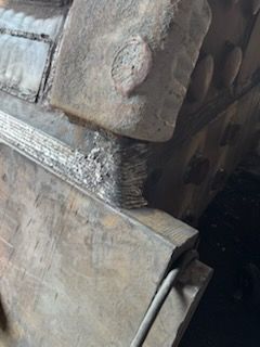 Close-up of a weathered, metallic structure with rough edges and a weld joint visible.