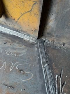 Welded metal corner with a yellow piece, showing weld lines.