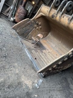 Excavator bucket, close-up, angled view, rusty metal, outdoor setting, construction equipment.