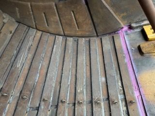 Close-up of worn metal components. Rows of vertical strips line a curved surface. Pink paint marks an edge.