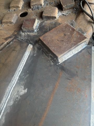 Metal fabrication with a large metal sheet, small metal blocks, and weld marks.