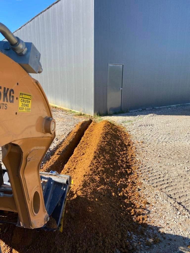A Machine Is Digging a Hole in The Ground in Front of A Building — St Elmo Contracting in Peelwood, NSW
