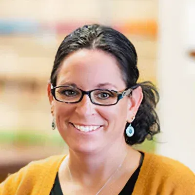 A woman wearing glasses and earrings is smiling for the camera.
