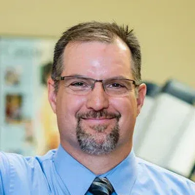 A man with a beard and glasses is wearing a blue shirt and tie.