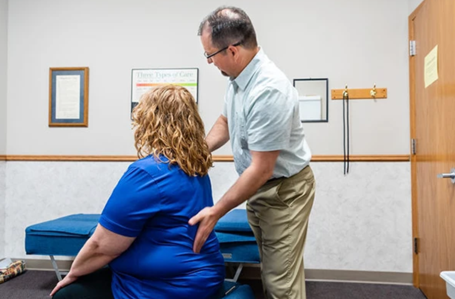 A man is stretching a woman 's arm while she sits on a table.