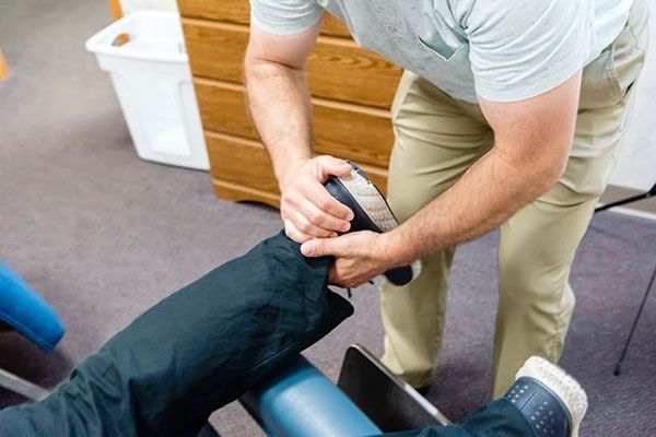 A man is stretching a person 's leg on a table.