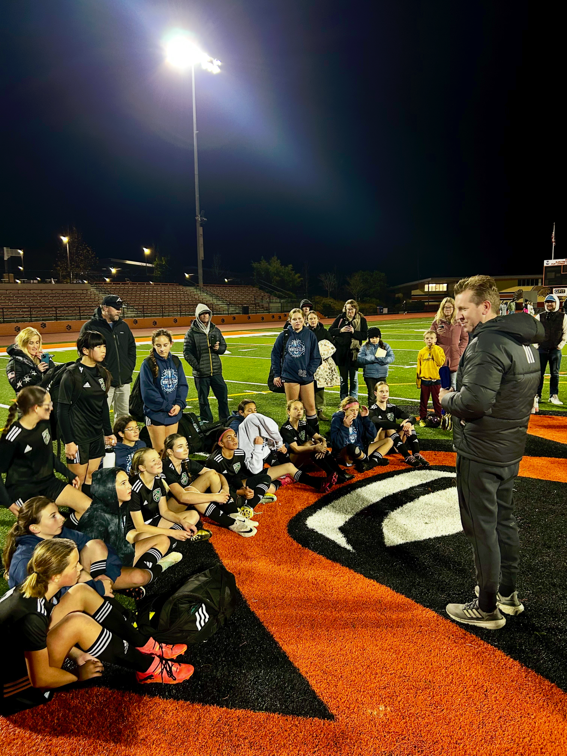 A man is talking to a group of people on a football field.