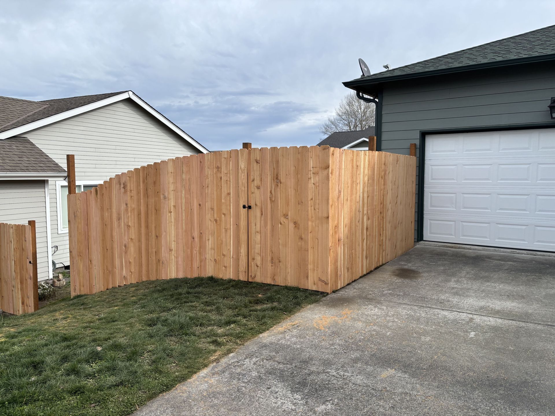 A wooden fence is sitting next to a garage door in front of a house.