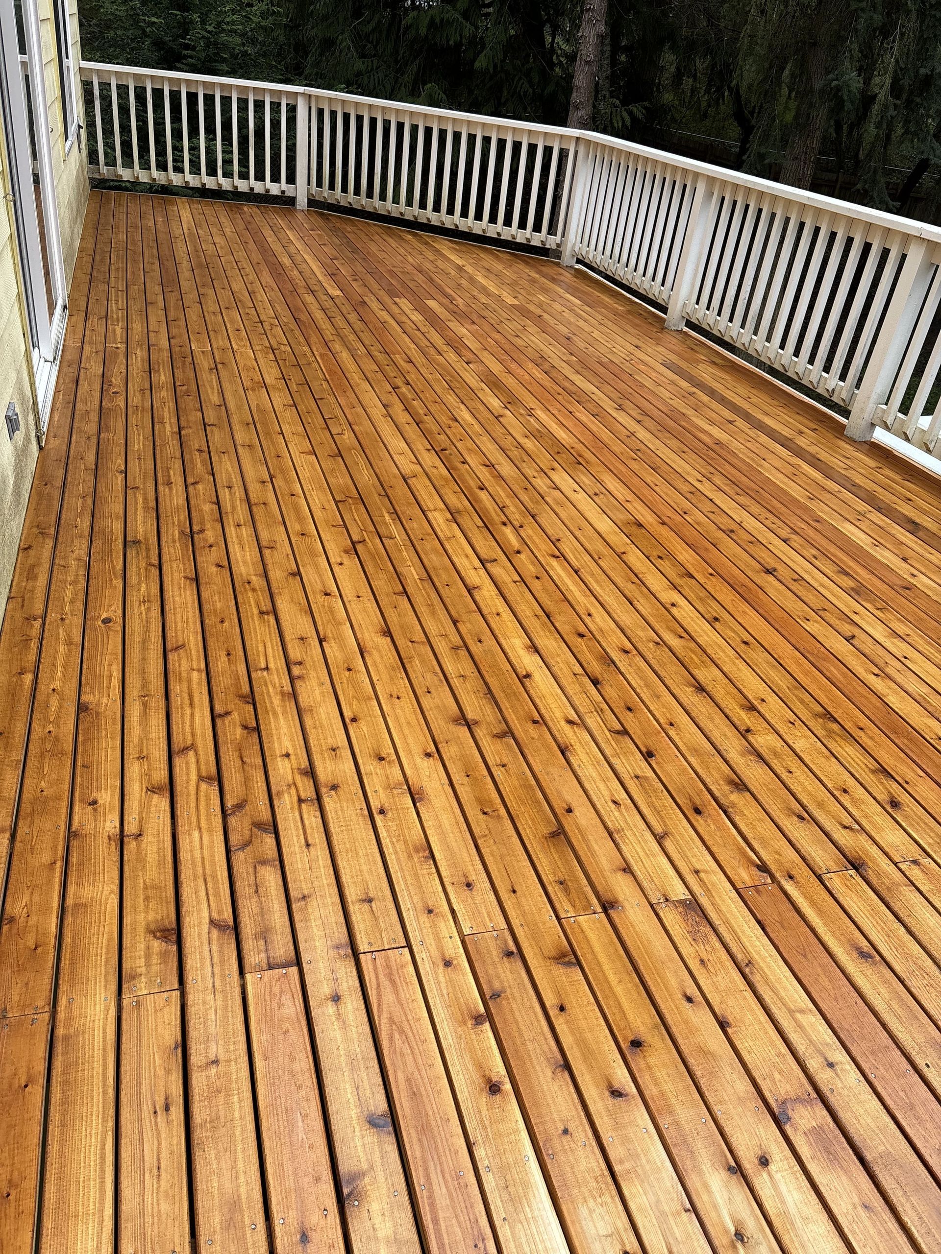 A large wooden deck with a white railing and trees in the background.