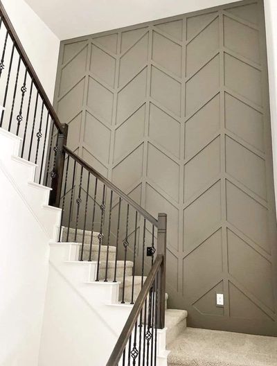 A stairwell wall featuring taupe-colored chevron molding, accented by a dark wood railing and a white staircase.