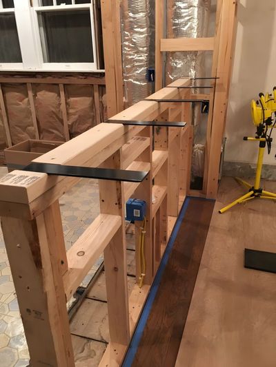 A half-wall frame with black metal countertop brackets installed on the top plate in an unfinished room.