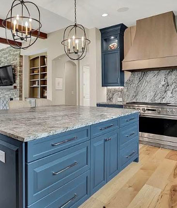 A bright kitchen features white cabinets, a farmhouse sink with a gold faucet, marble-style countertops, and wood floors.