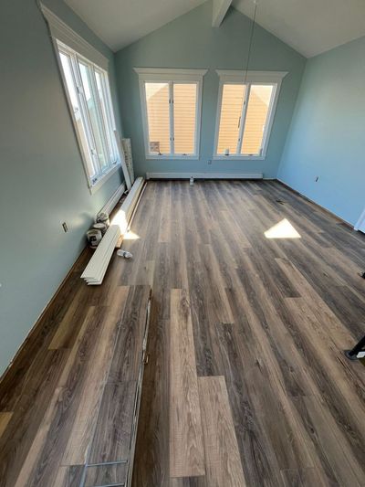 A sunlit room with pale blue walls and new, multi-toned wood-look plank flooring partially installed over a baseboard.