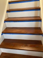 A set of wooden stairs with white risers. Blue painter's tape is applied along the edges of the steps for renovation.