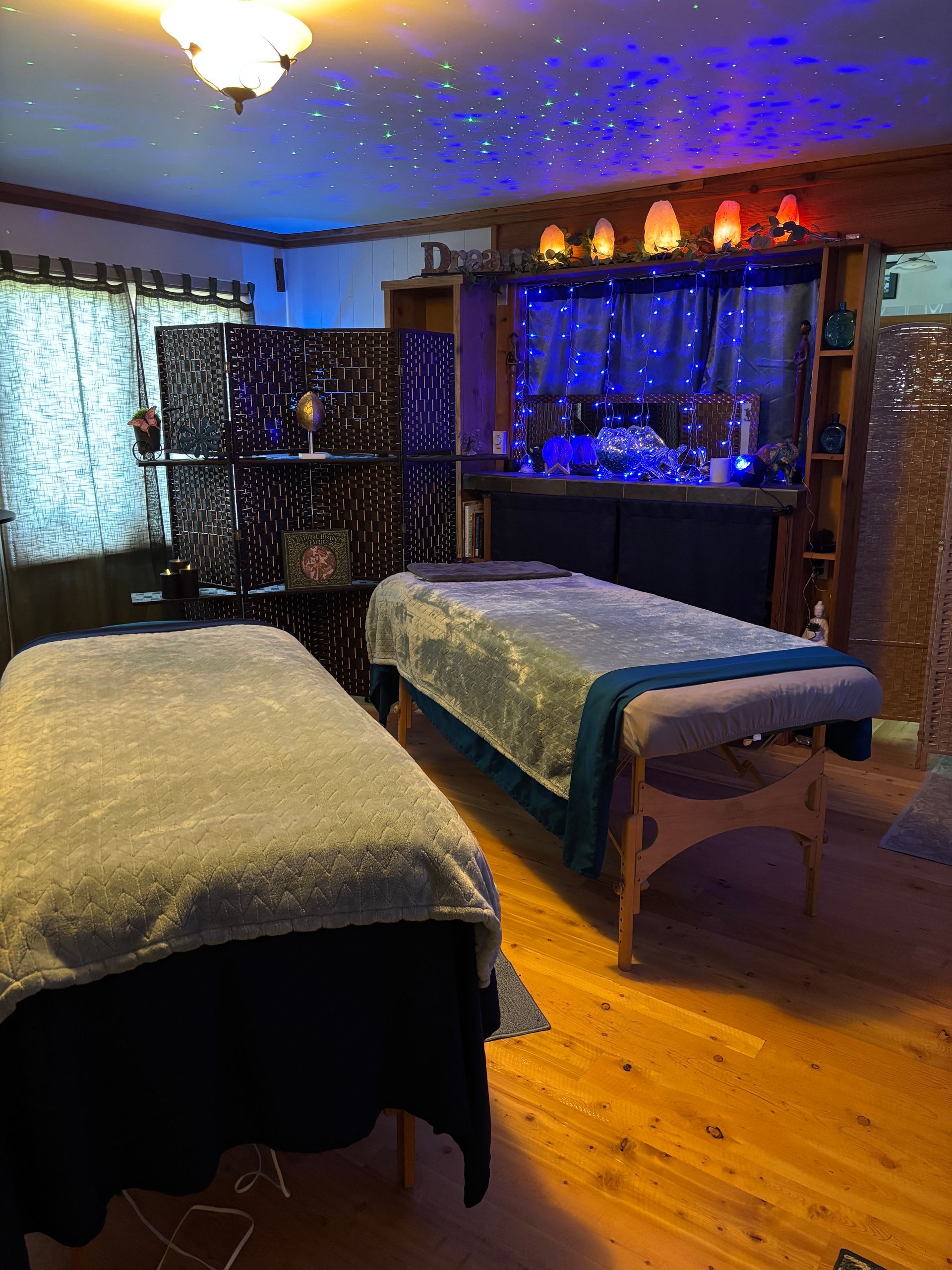 Two massage tables in a dimly lit room with star-like ceiling lights and blue accents.