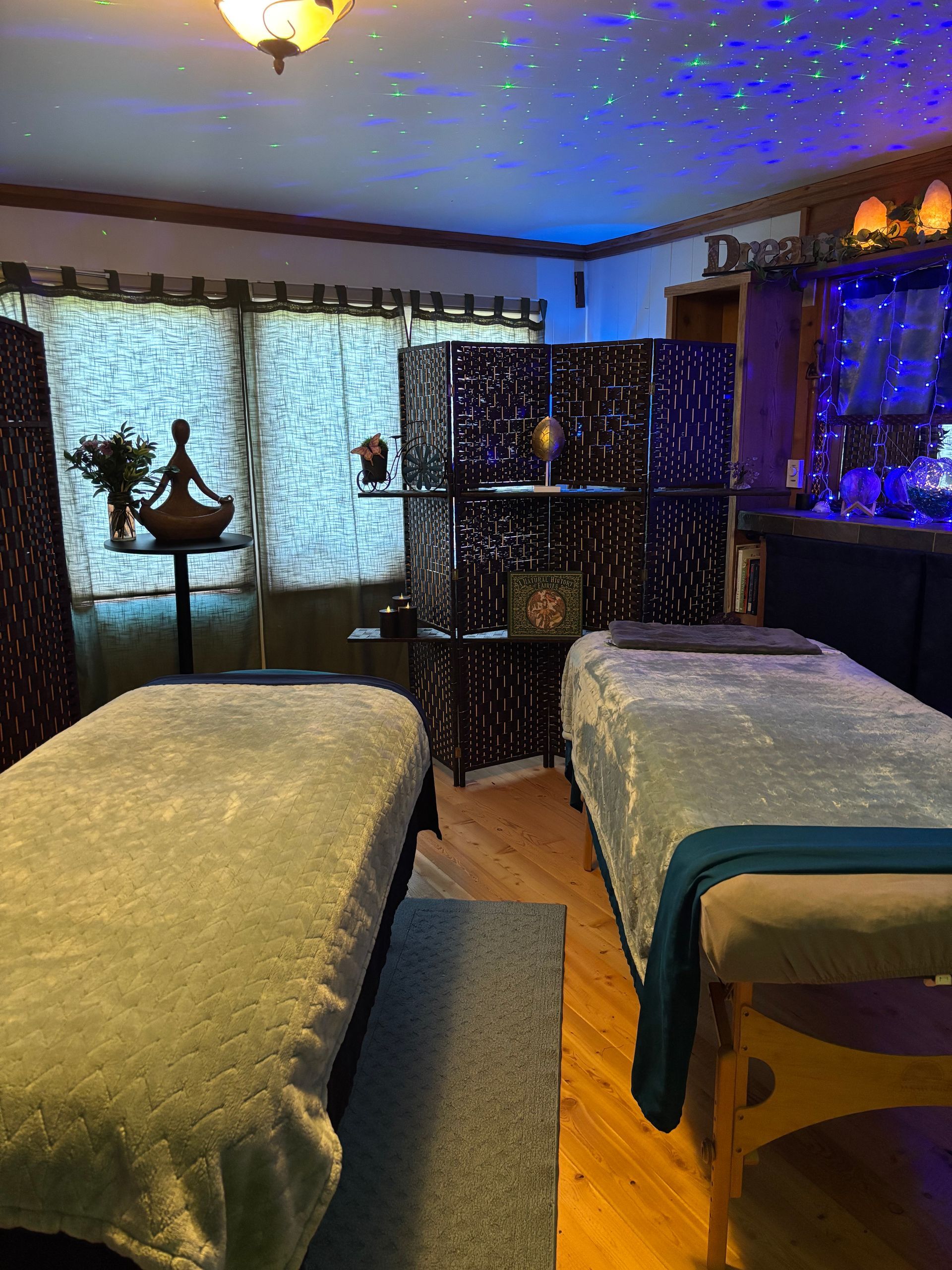 Two massage tables in a dimly lit room with star-like ceiling lights and a dark wooden divider.