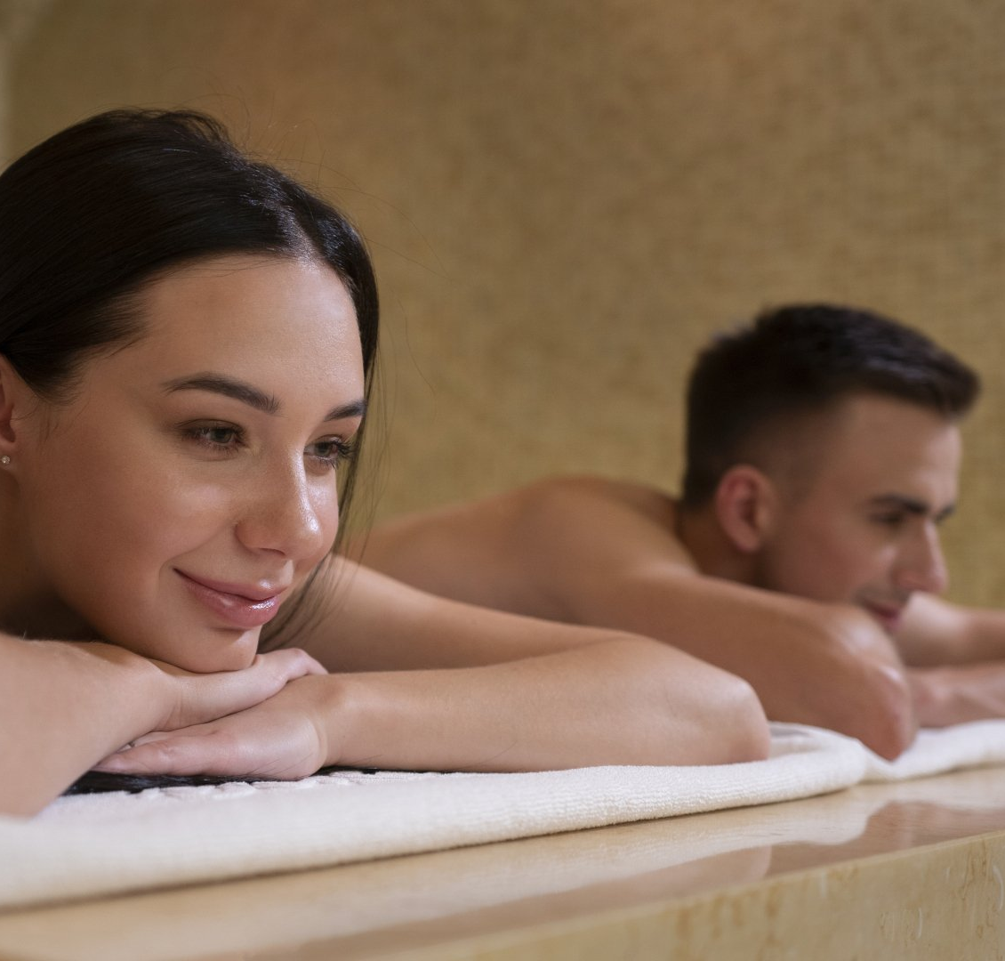 Woman and man relaxing at a spa, lying on a towel, smiling, indoors.