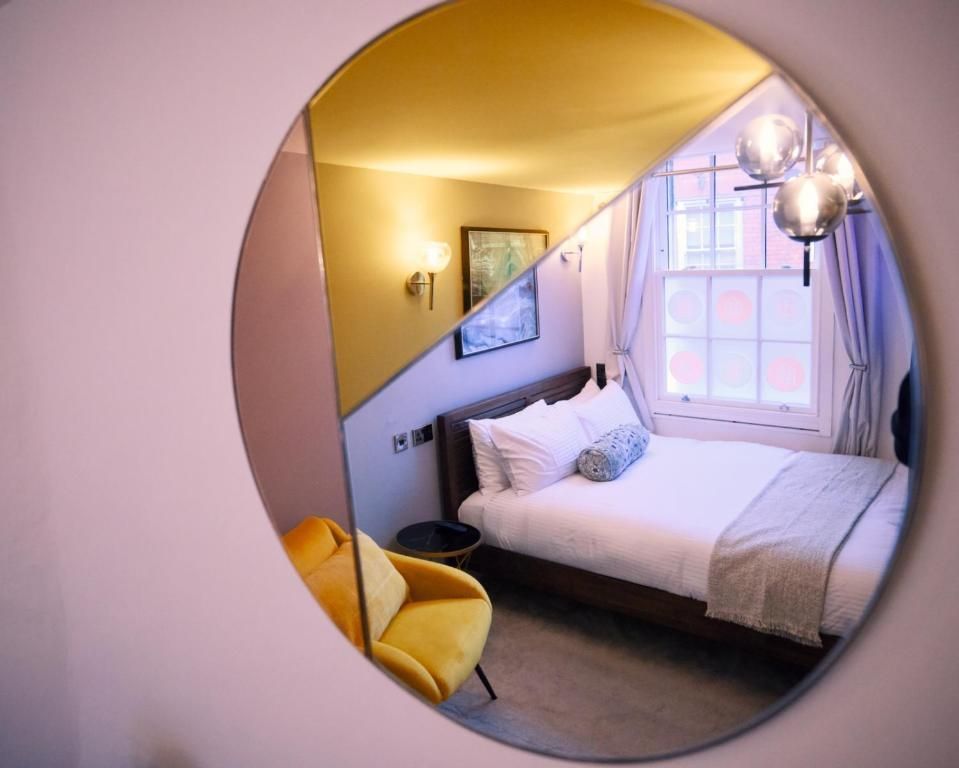 Circular mirror reflecting a bedroom with a bed, chair, and window.