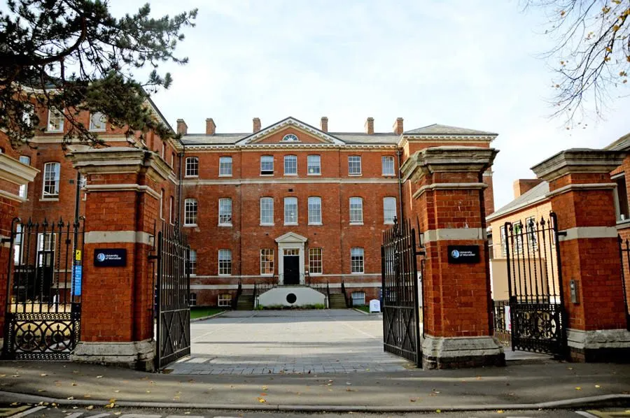 Red brick building with open black iron gates. A paved courtyard is in front of the building.