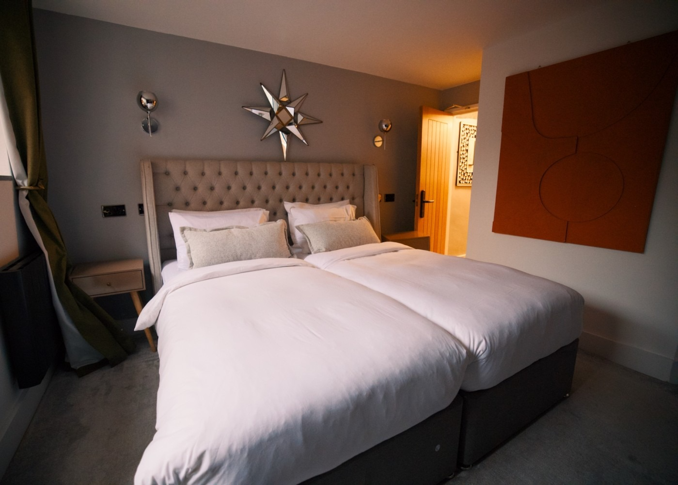 Bedroom with two twin beds, gray walls, starburst mirror, and orange artwork.