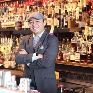 a man in a suit and hat is standing in front of a bar full of liquor bottles .