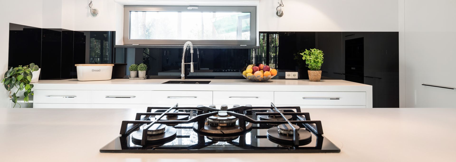 Modern kitchen with a sleek white countertop and black splashback and a gas stove in the foreground.