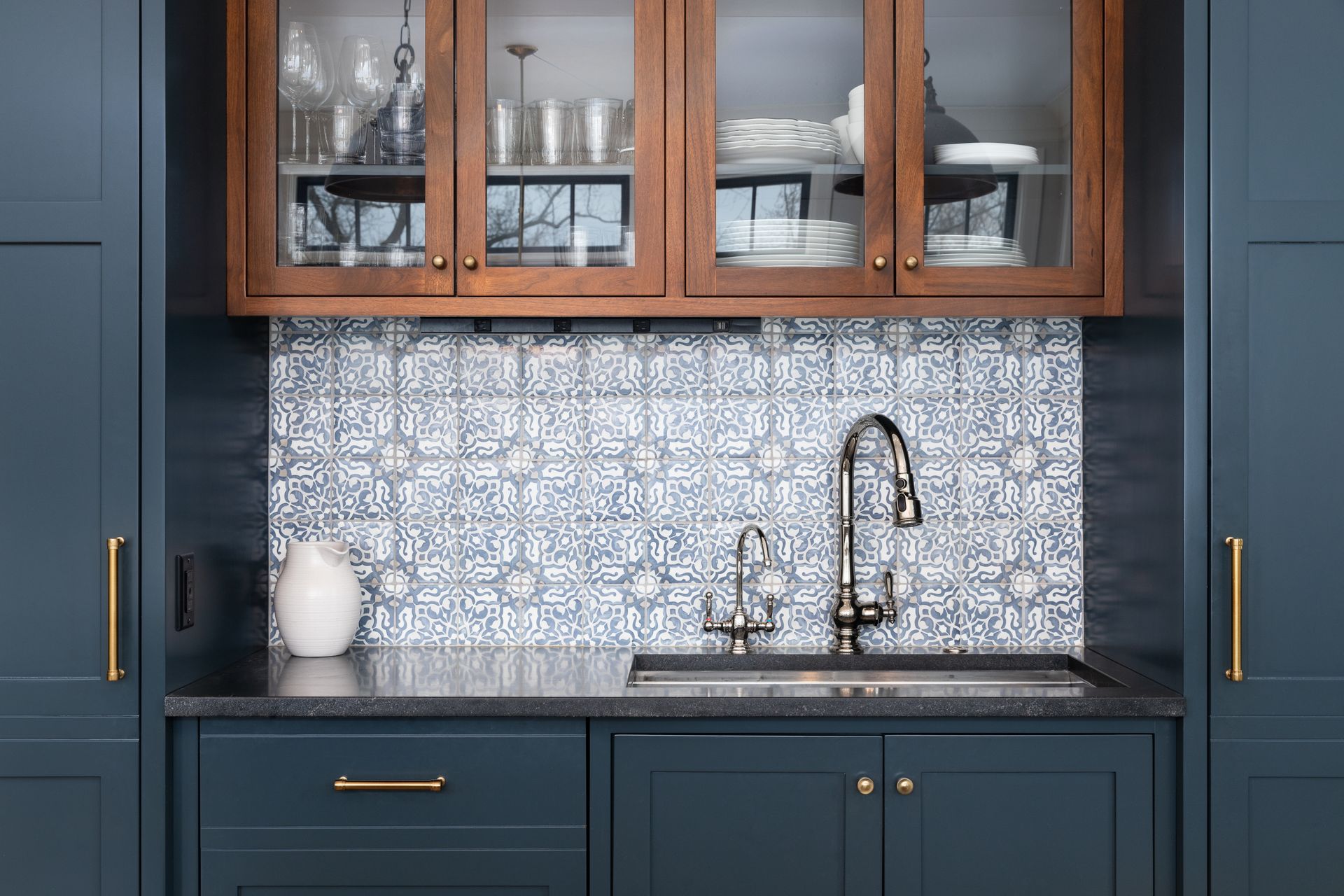 A kitchen sink with a tiled glass splashback, a chrome faucet, and blue and wood cabinets. A kitchen sink with a tiled glass splashback, a chrome faucet, and blue and wood cabinets.