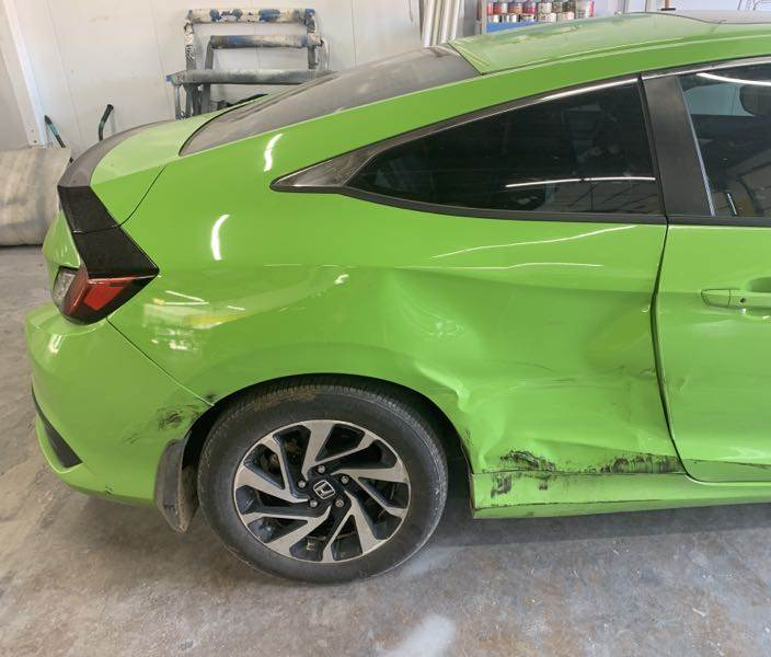 A green car with a damaged side is parked in a garage.