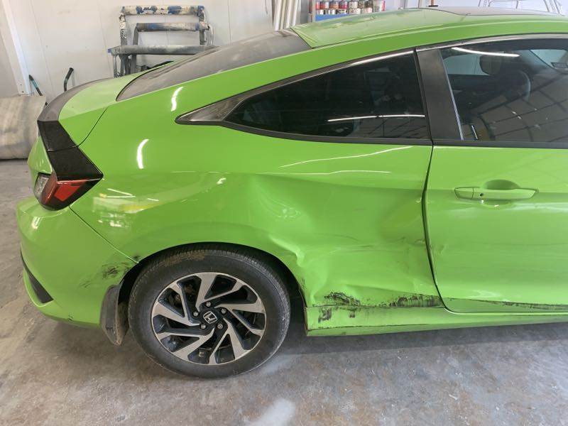 A green car with a damaged side is parked in a garage.