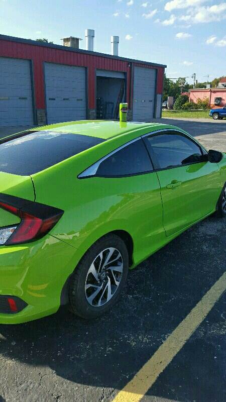 A green car is parked in a parking lot in front of a garage.