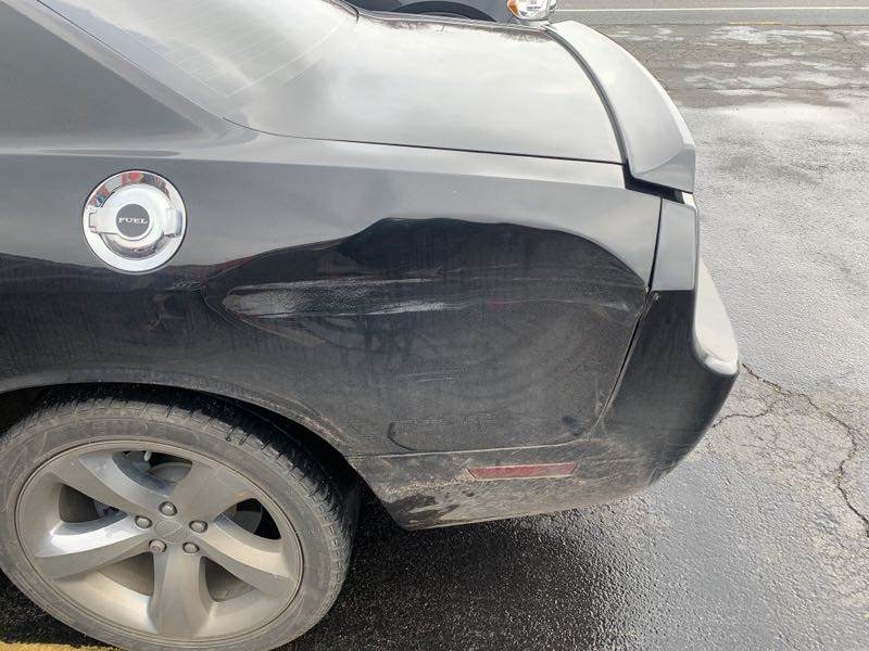 A black car with a damaged fender is parked in a parking lot