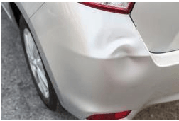 A silver car with a damaged bumper is parked on the side of the road.