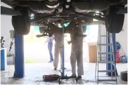 Two mechanics are working under a car in a garage.