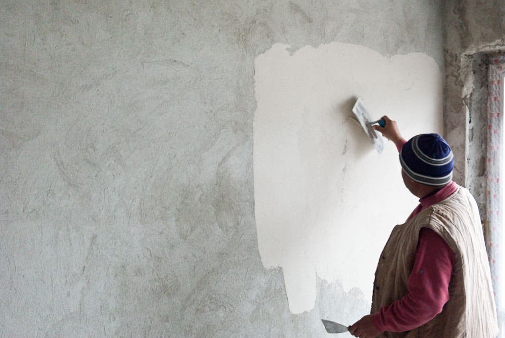 man applying stucco to a grey wall