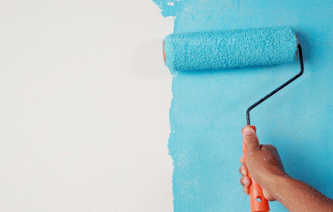 A person is painting a wall blue with a paint roller.