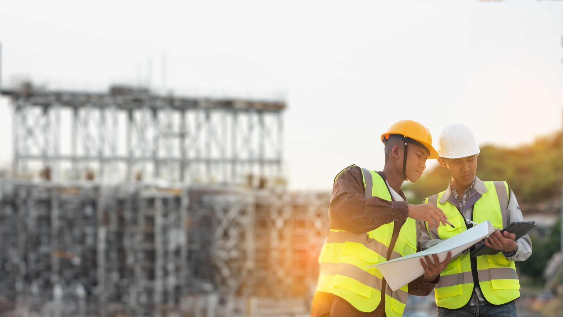 Two construction workers in yellow safety vests and hard hats reviewing plans at a job site