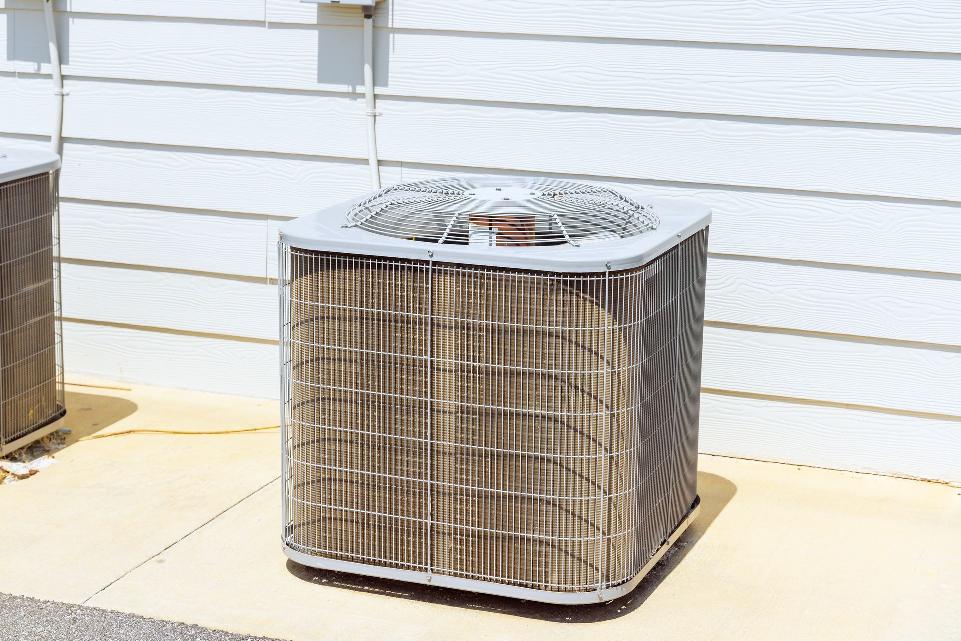 An air conditioning unit outside a white-sided house on a sunny day.