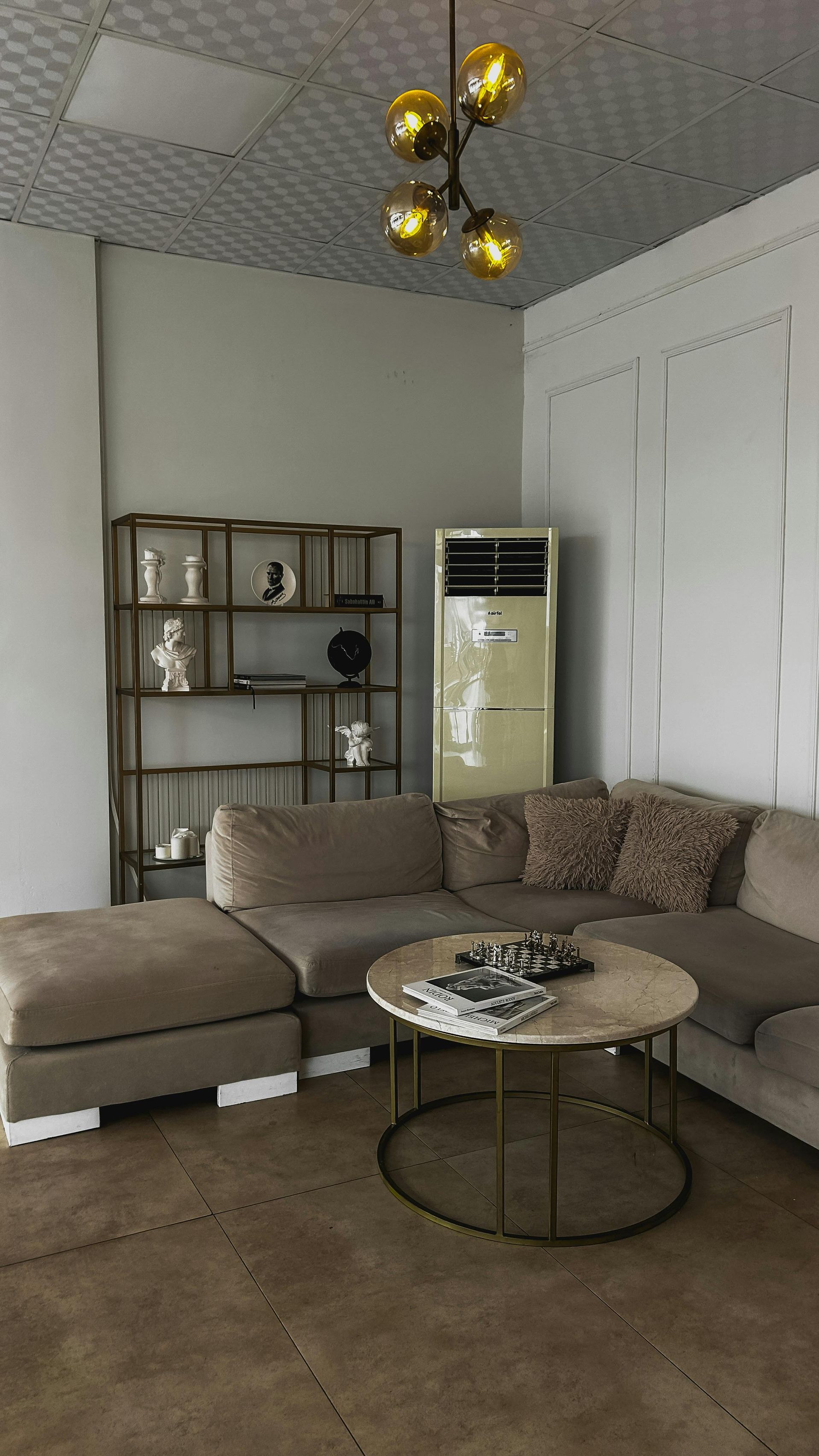Living room with sectional sofa, coffee table, and bookshelf. Tan and brown tones.