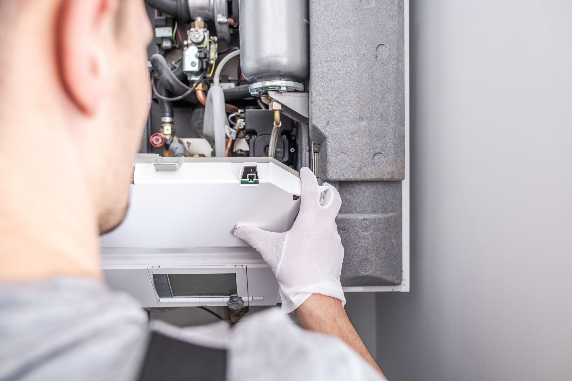 Technician in white gloves inspecting an open wall-mounted boiler control panel.