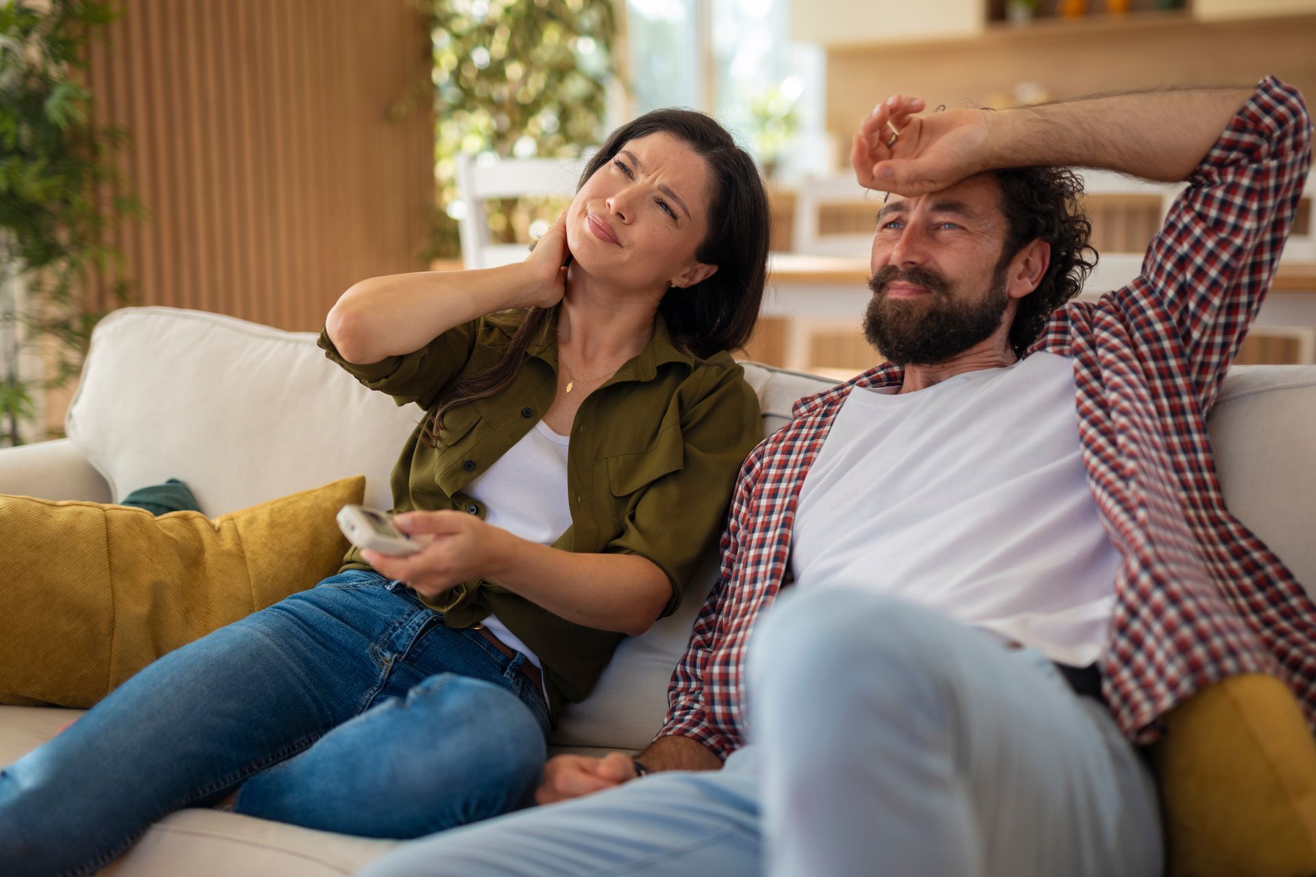 Woman holding neck and man relaxing on couch in living room.