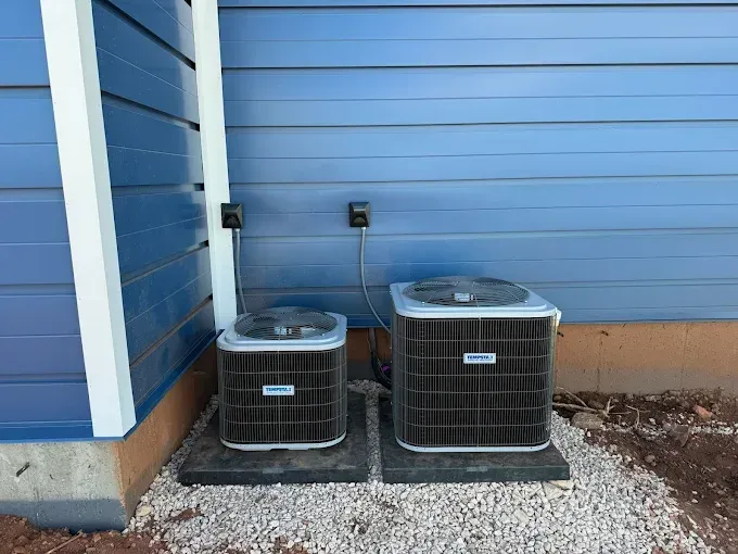 Two air conditioners are sitting outside of a blue house.