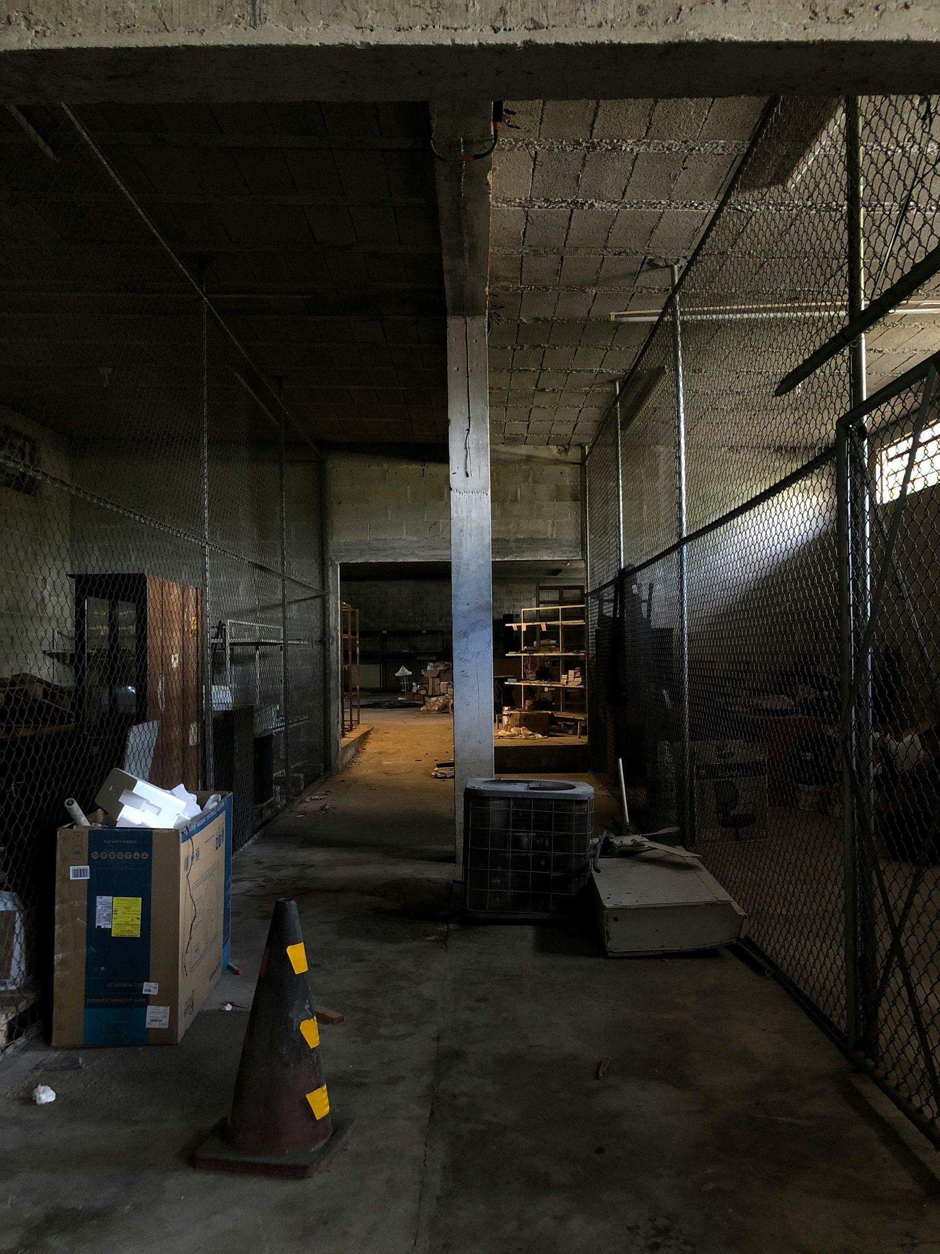 An empty warehouse with a chain link fence and a cone in the middle.