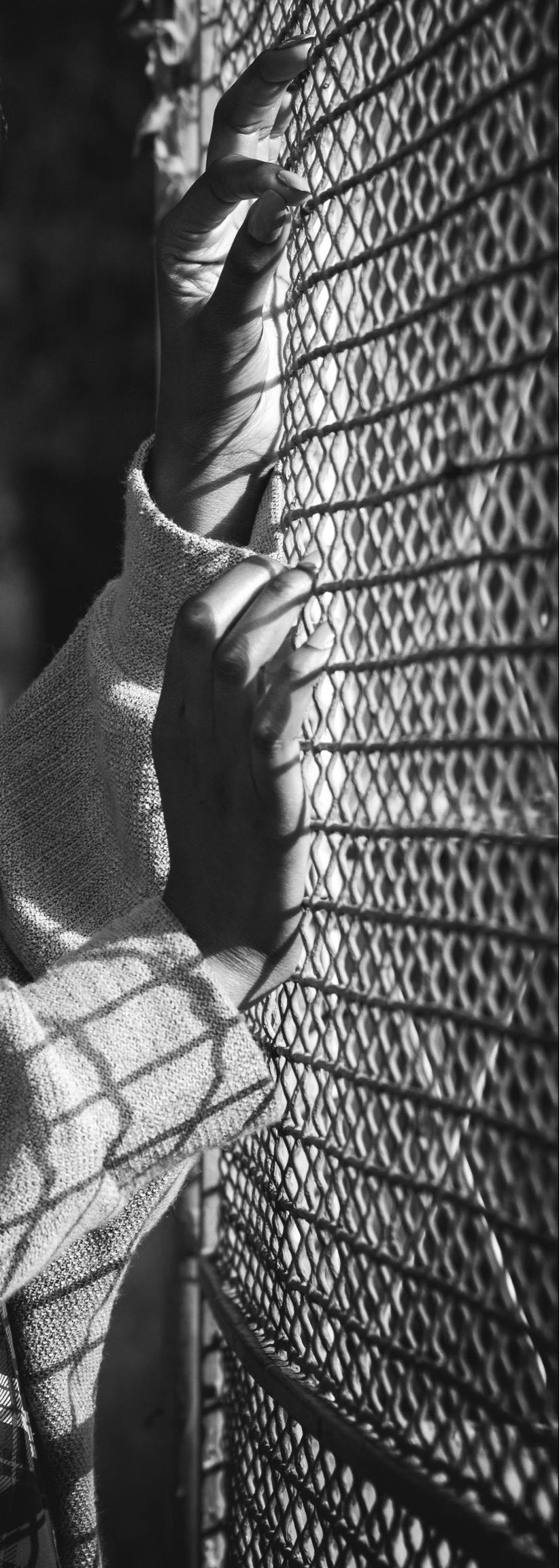 A black and white photo of a person standing in front of a fence.
