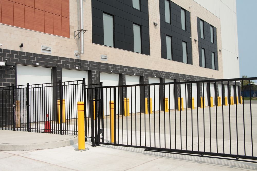 A large building with a black fence and yellow poles in front of it.