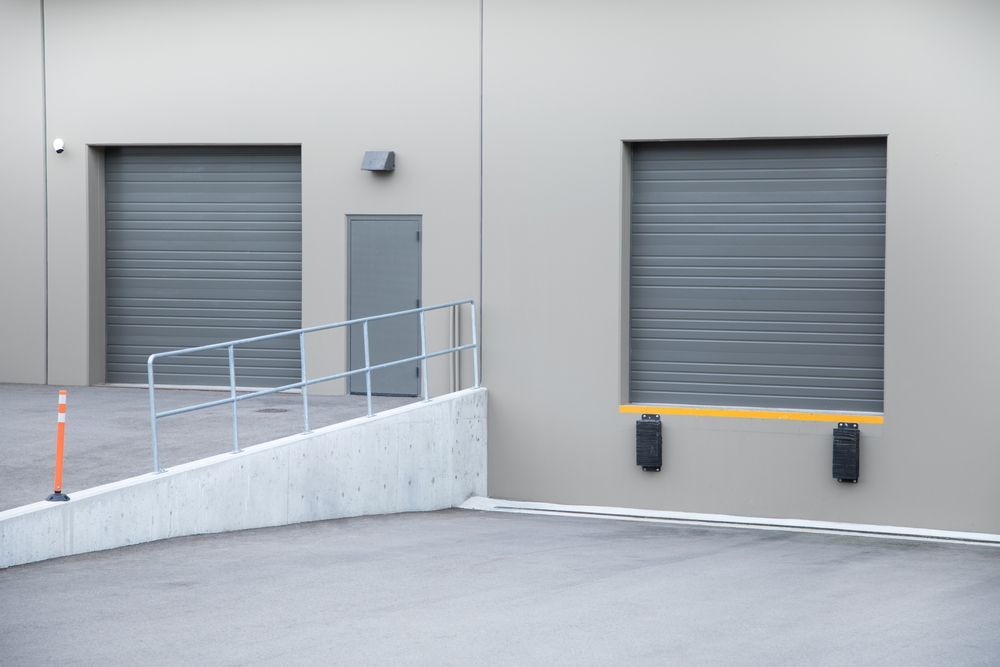 A ramp leading to a warehouse with two garage doors and a door.
